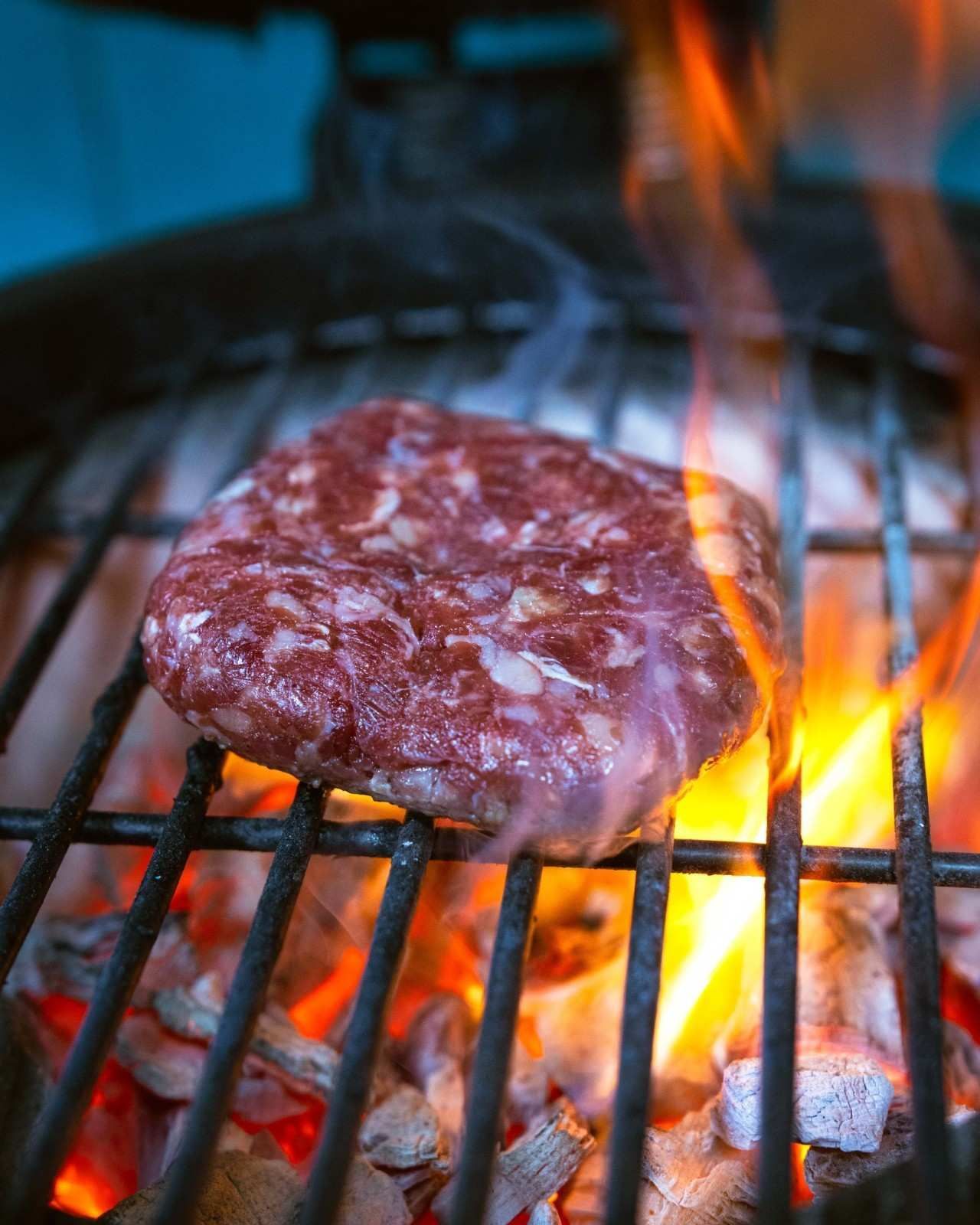 Hamburguesa cruda en una parrilla caliente, con llamas elevándose.