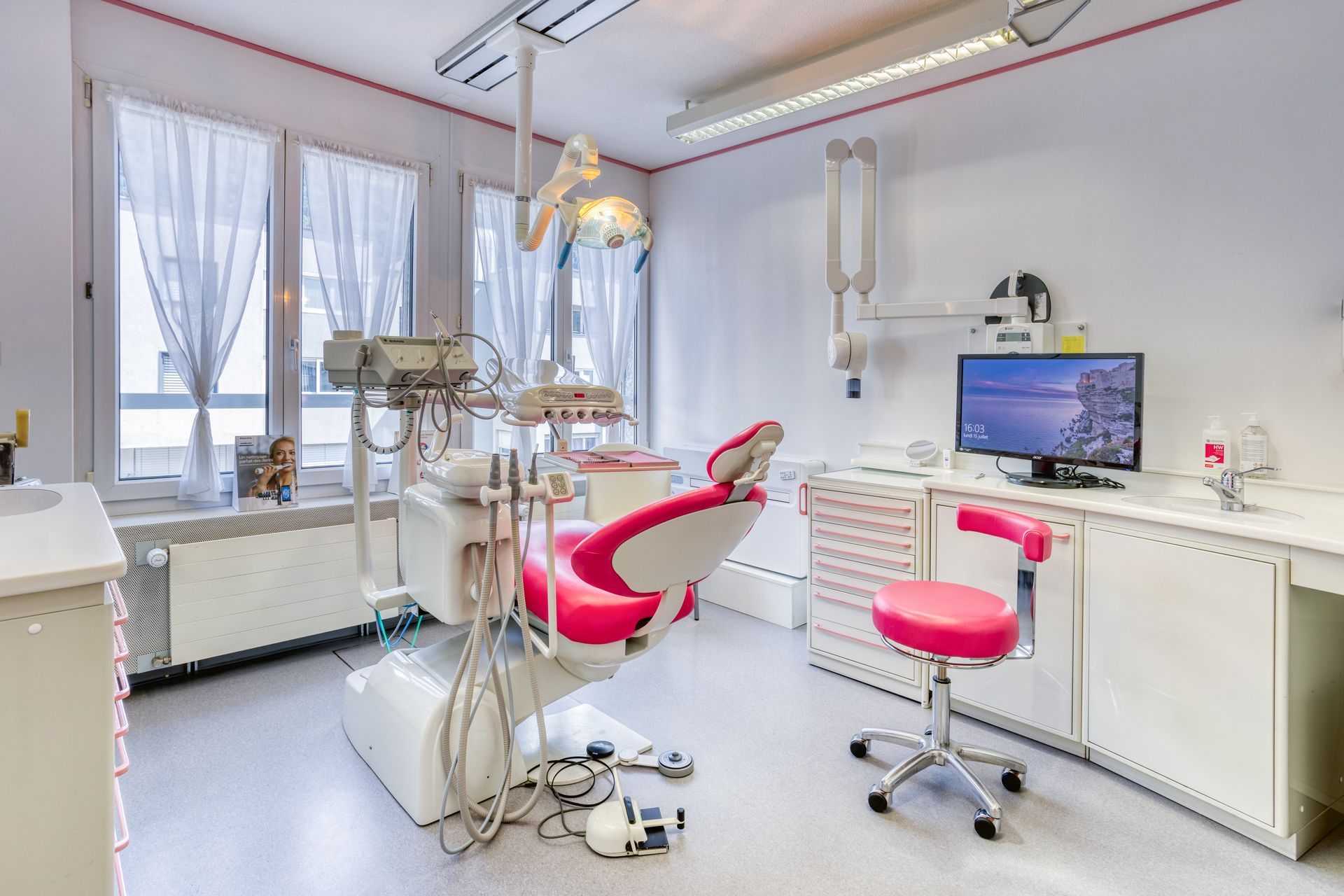 Un cabinet dentaire avec une chaise rose et un ordinateur.