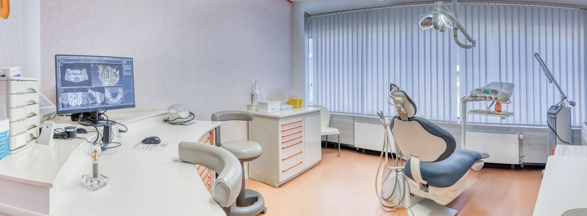 Un cabinet dentaire avec une chaise dentaire, un bureau, un moniteur et d'autres équipements dentaires.