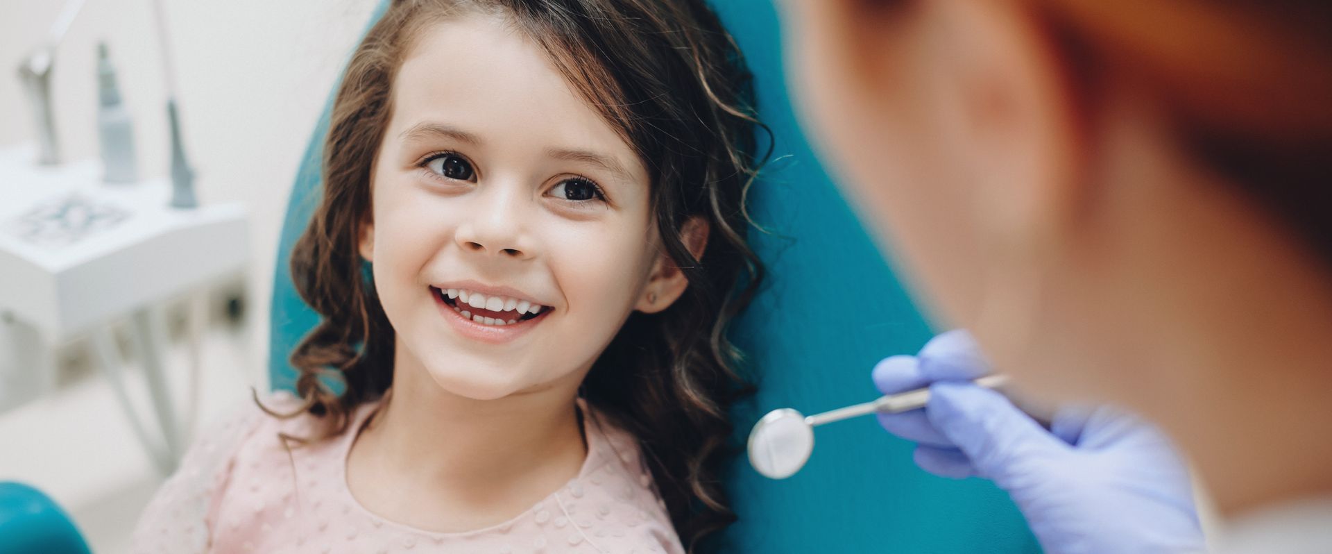 Une petite fille est assise sur une chaise dentaire pendant qu'un dentiste examine ses dents.