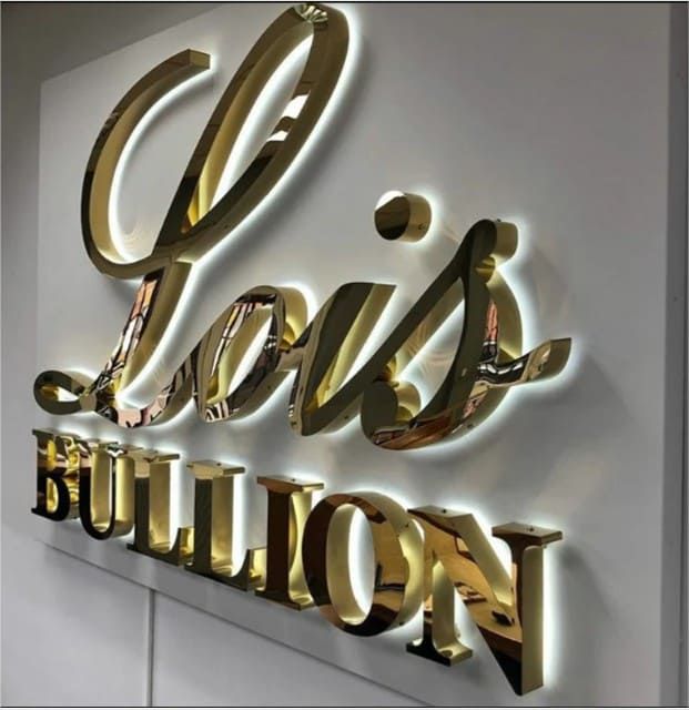 Letras corpóreas tridimensionales de color dorado brillante con retroiluminación blanca sobre una pared blanca, que muestran el texto