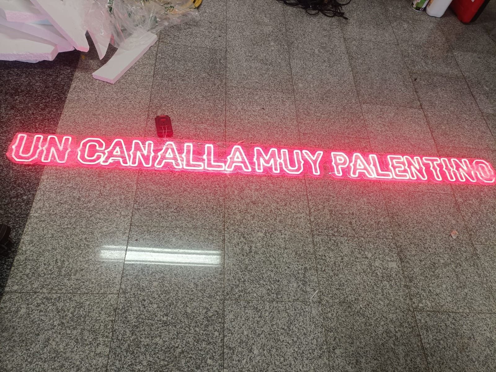 A pink neon sign on a gray tiled floor that reads: