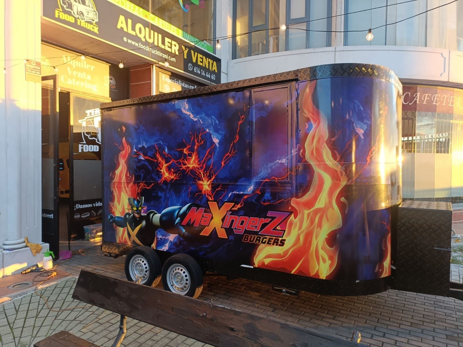 Un remolque decorado con un llamativo gráfico de Mazinger Z con elementos de fuego y relámpagos, estacionado frente a una tienda.