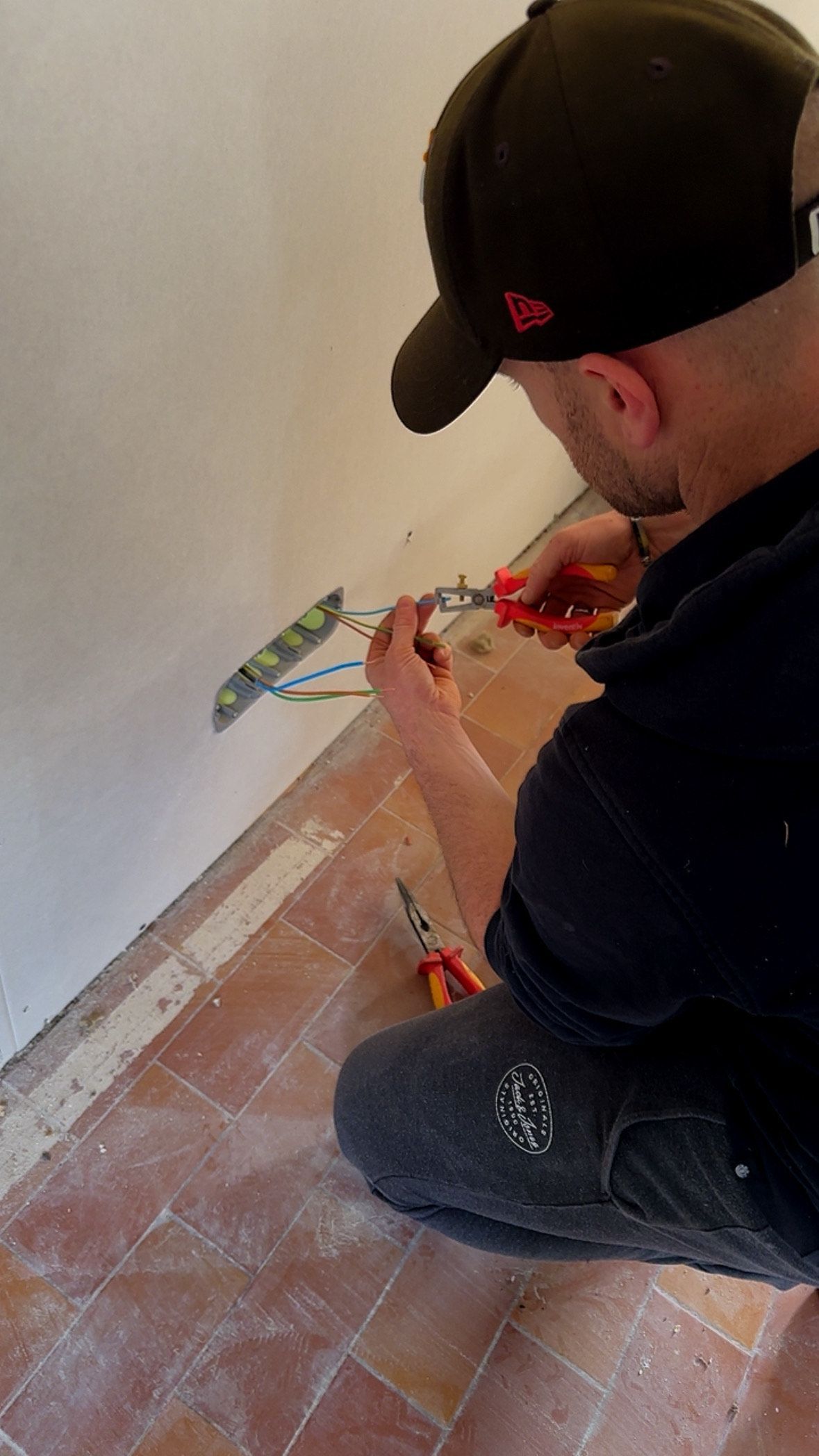 Électricien en gants bleus, câble une prise de courant avec un multimètre.