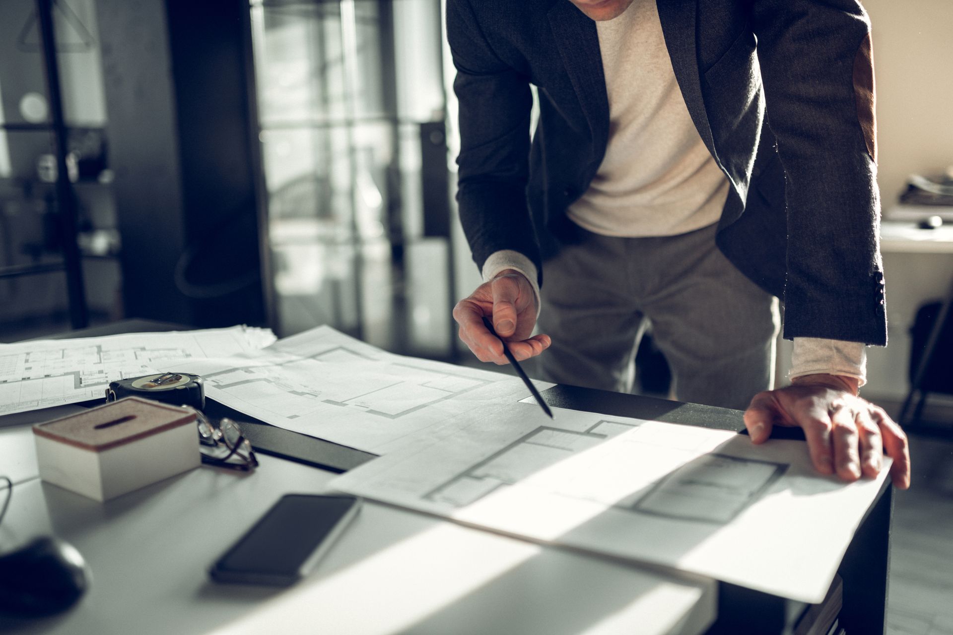Un homme en blazer montre des plans architecturaux sur un bureau dans un bureau.