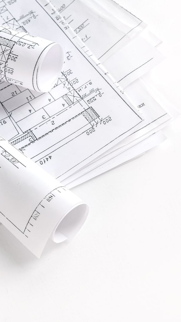 Plans architecturaux, roulés et empilés, sur une surface blanche.