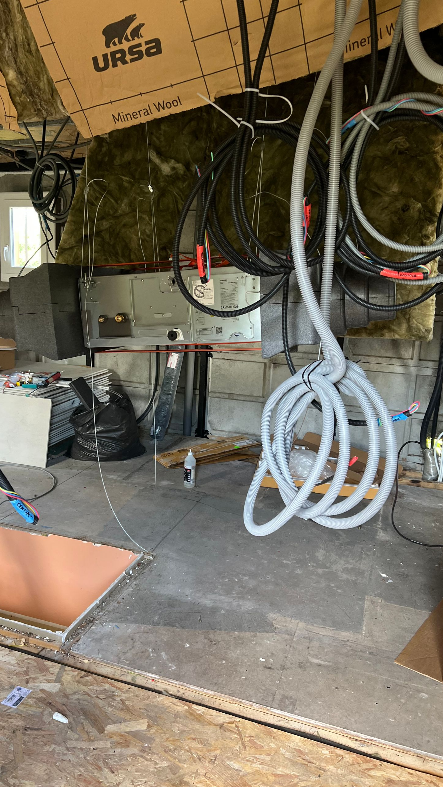 Intérieur du sous-sol avec isolation apparente, câblage électrique et matériaux de construction éparpillés.