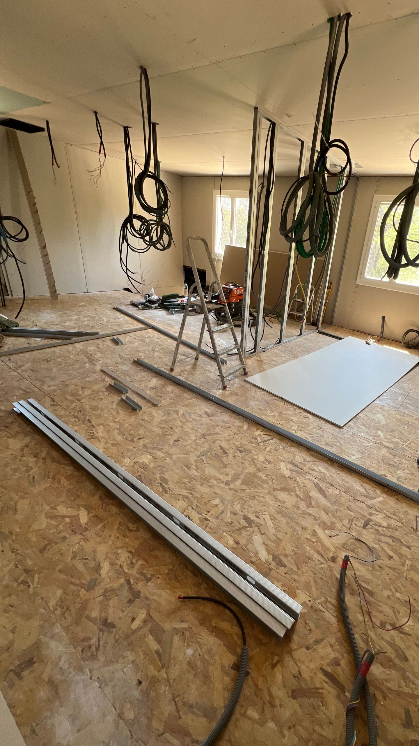 Chantier de construction intérieur avec câblage exposé, cloisons sèches, outils et plancher de bois.