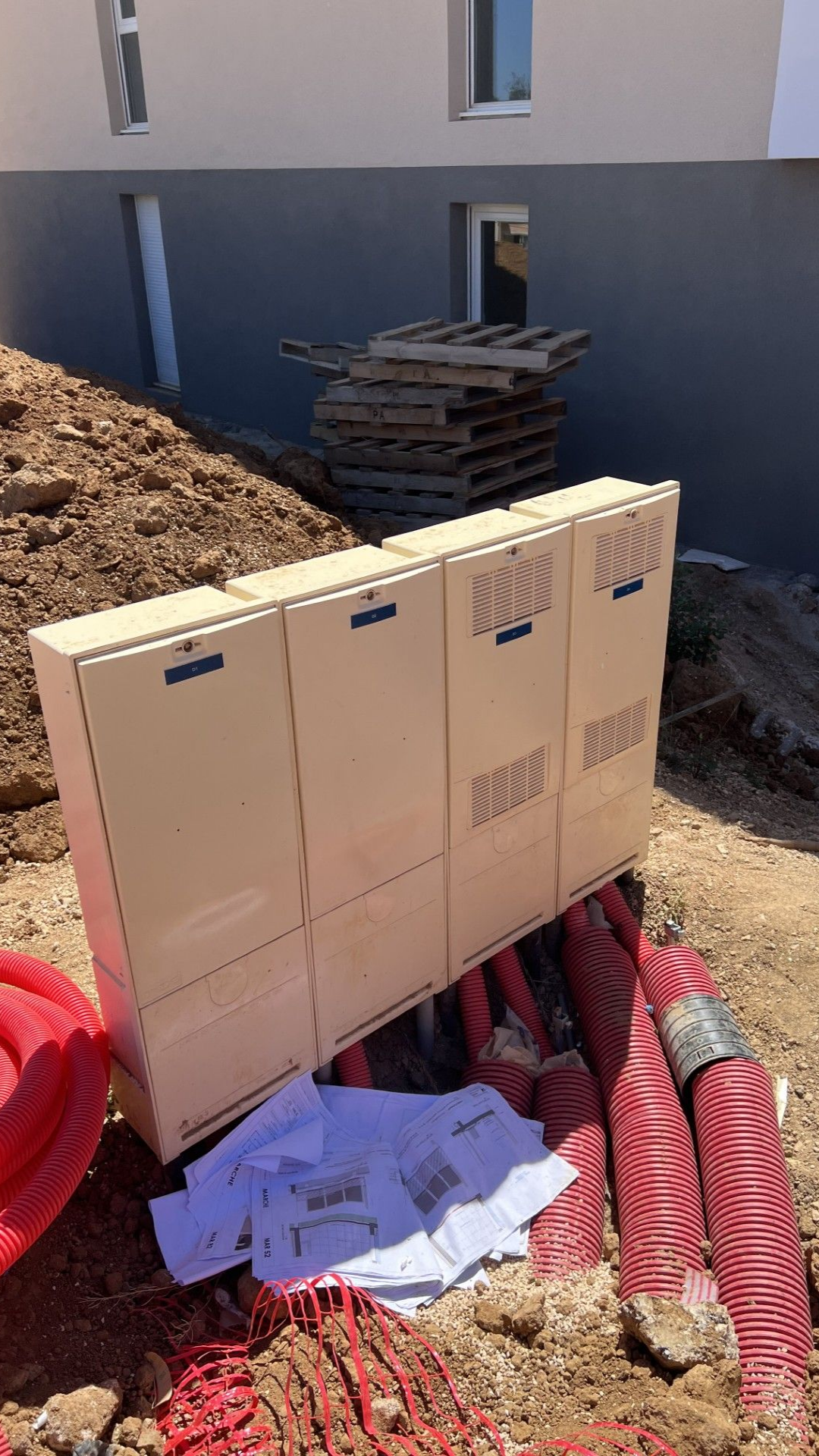 Coffrets électriques à l'extérieur d'un bâtiment, avec conduit rouge et papiers au sol.