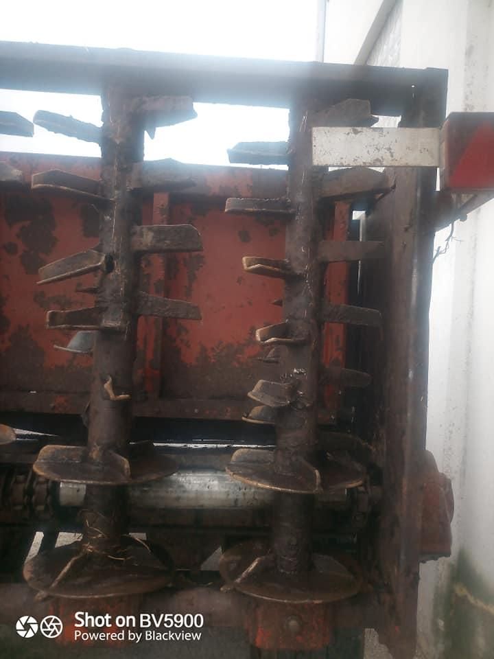 Distribuidor de estiércol oxidado y rojo, con sinfines verticales, en un cobertizo.