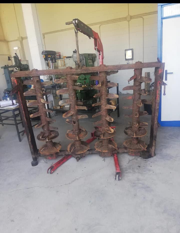 Una grada de discos agrícola oxidada en un taller, marco de soporte rojo, marco de metal y púas.