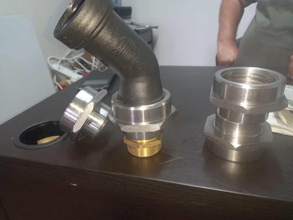 Accesorio de tubería negro con dos piezas de metal sobre una superficie de madera oscura.