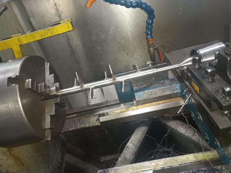 Una varilla metálica con aletas se sujeta en un torno y se mecaniza en un taller.