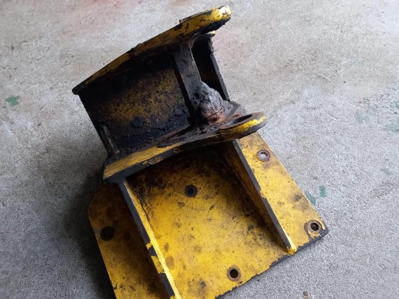 Soporte de metal amarillo con placa de montaje, cubierto de suciedad y aceite.