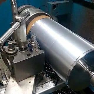 Un cilindro de metal siendo mecanizado en un torno; virutas visibles.
