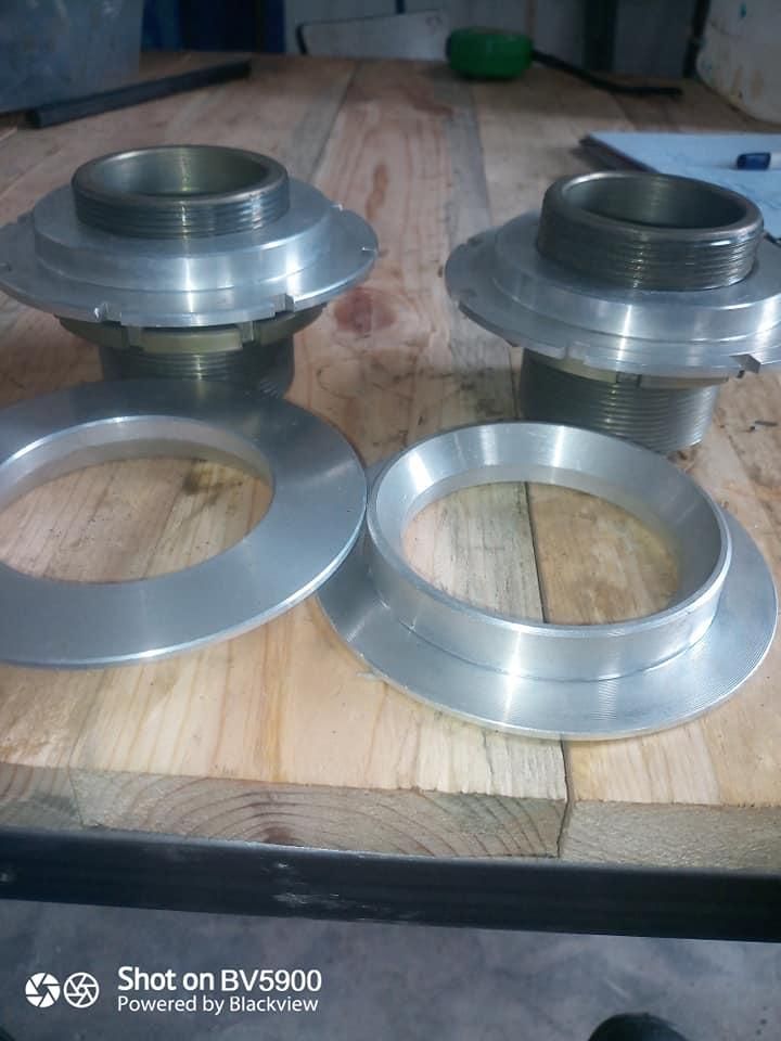 Dos cubos roscados de metal y dos anillos circulares de metal sobre una superficie de madera.