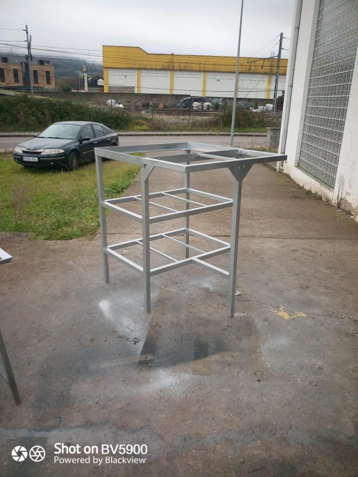 Estantería metálica sobre hormigón; coche negro y edificio al fondo.