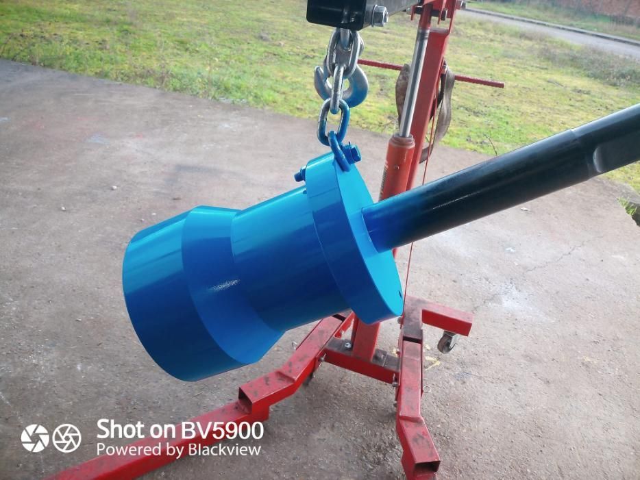 Un cilindro metálico pintado de azul, suspendido por una grúa, sostiene un tubo negro