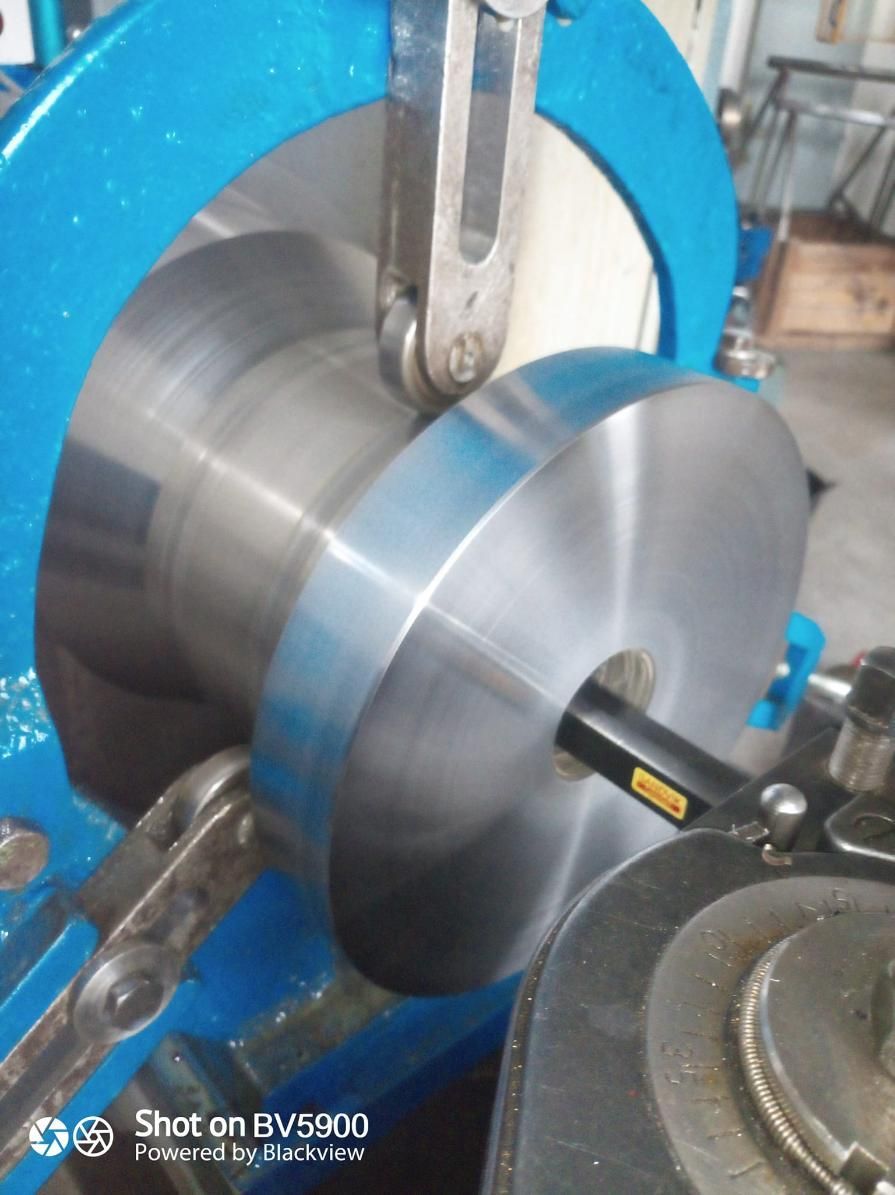 Un disco metálico moldeado por maquinaria. Presenta tonos azules y plateados. Se está realizando un torneado.