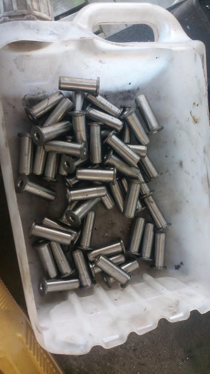 Pila de alfileres metálicos cilíndricos en un recipiente de plástico blanco, probablemente para uso industrial.