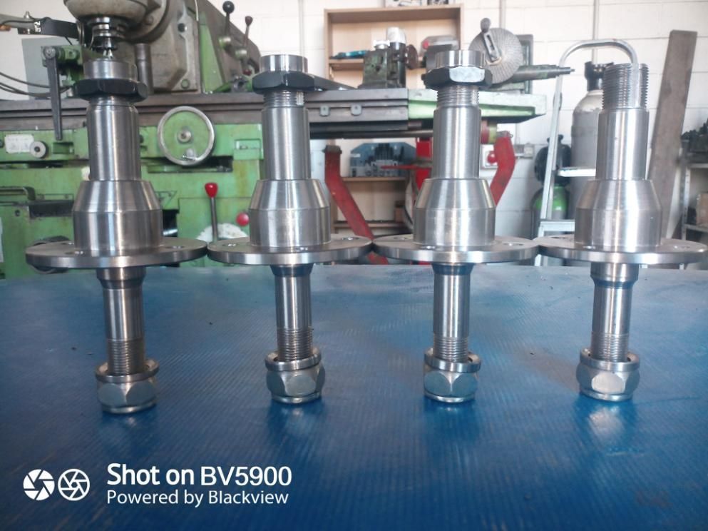 Cuatro husillos metálicos brillantes con tuercas y arandelas, delante de un taller.