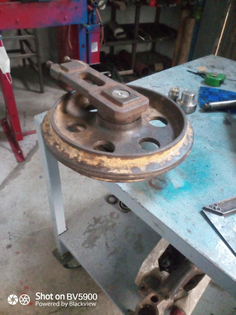 Rueda de metal oxidada con mango, colocada sobre una mesa con tapa azul en un entorno de taller.