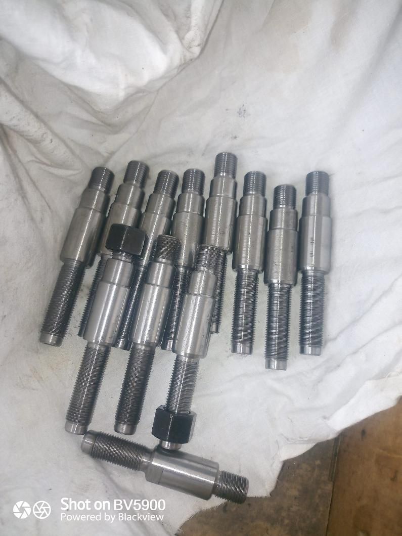 Una pila de ejes cilíndricos de metal con extremos roscados y secciones texturizadas