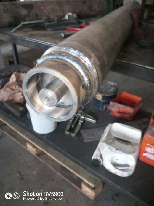 Un tubo de metal con un impulsor soldado, colocado sobre un banco de trabajo en un taller.