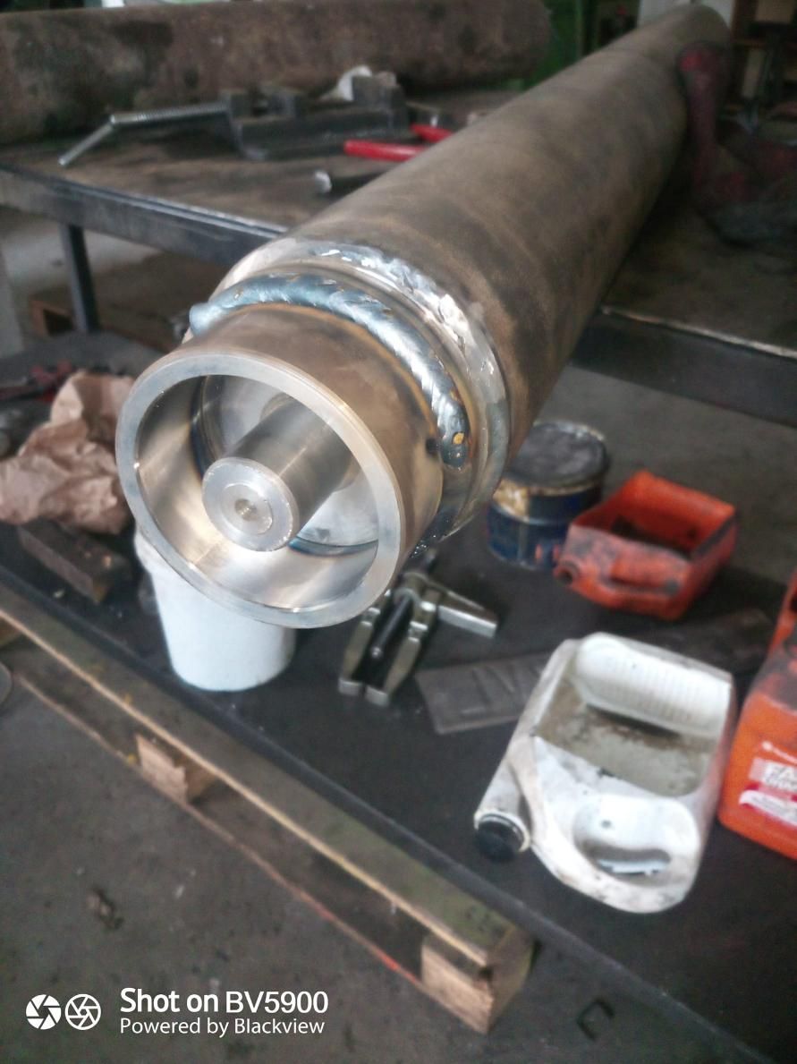 Cilindro metálico con impulsor soldado, sobre una mesa de taller rodeado de herramientas y contenedores.