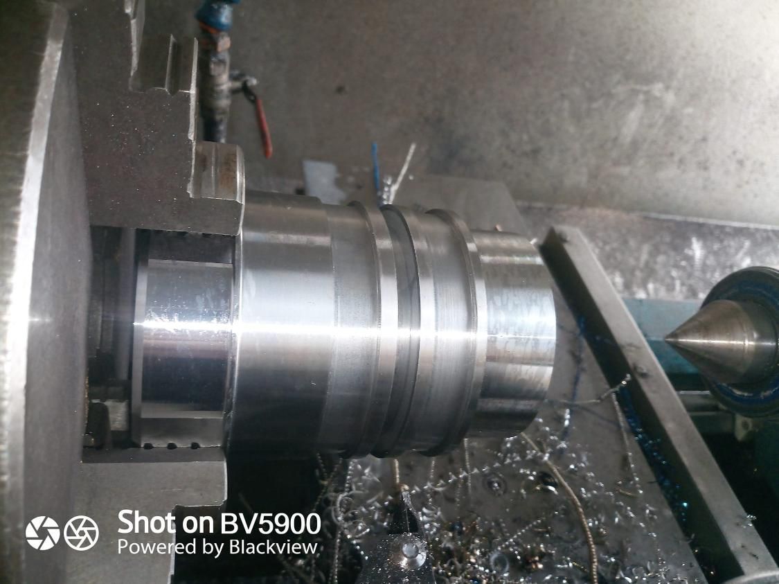 Un cilindro de metal siendo mecanizado en un torno; virutas visibles.