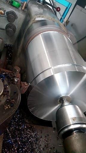 Un gran cilindro metálico en un torno en proceso de mecanizado. Virutas de metal rodean la máquina.