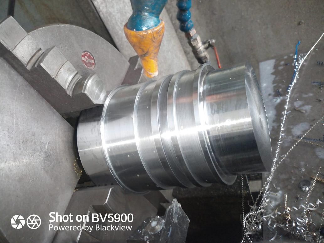 Una pieza de metal cilíndrica que se mecaniza en un torno; se le rocían refrigerantes.