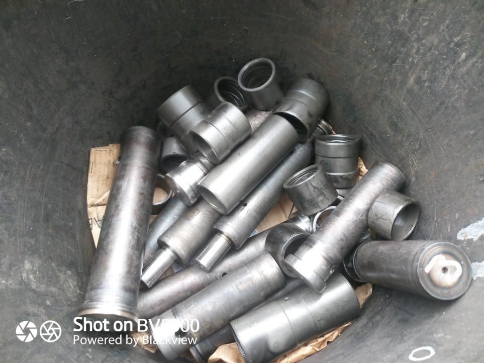 Pila de varias piezas cilíndricas de máquinas metálicas dentro de un contenedor oscuro.