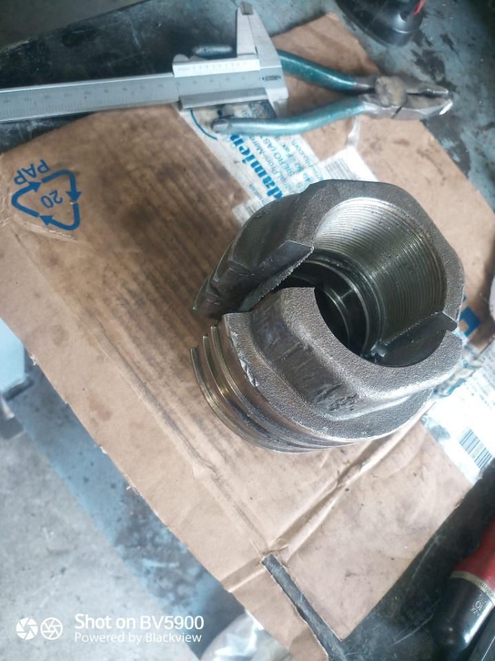 Pieza metálica rota con roscas internas, tirada sobre un cartón con herramientas cerca.