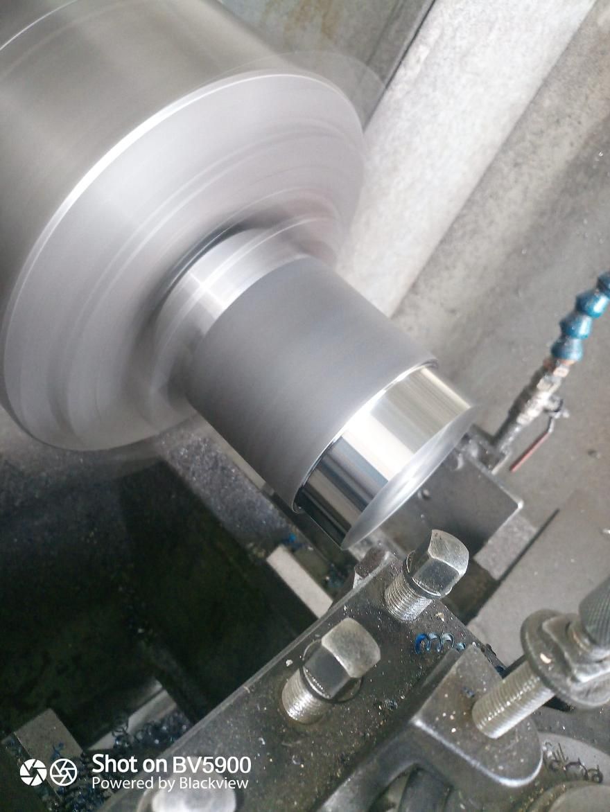 Cilindro metálico en un torno, en proceso de mecanizado. Boquilla de refrigerante presente.