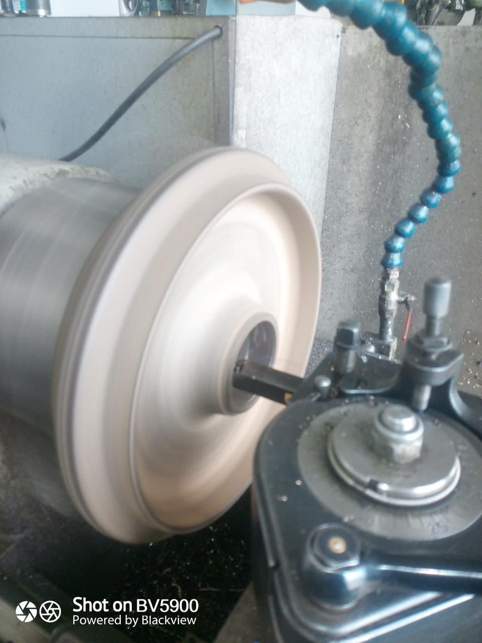 Una rueda de metal giratoria mecanizada en un torno. Manguera de refrigerante visible.