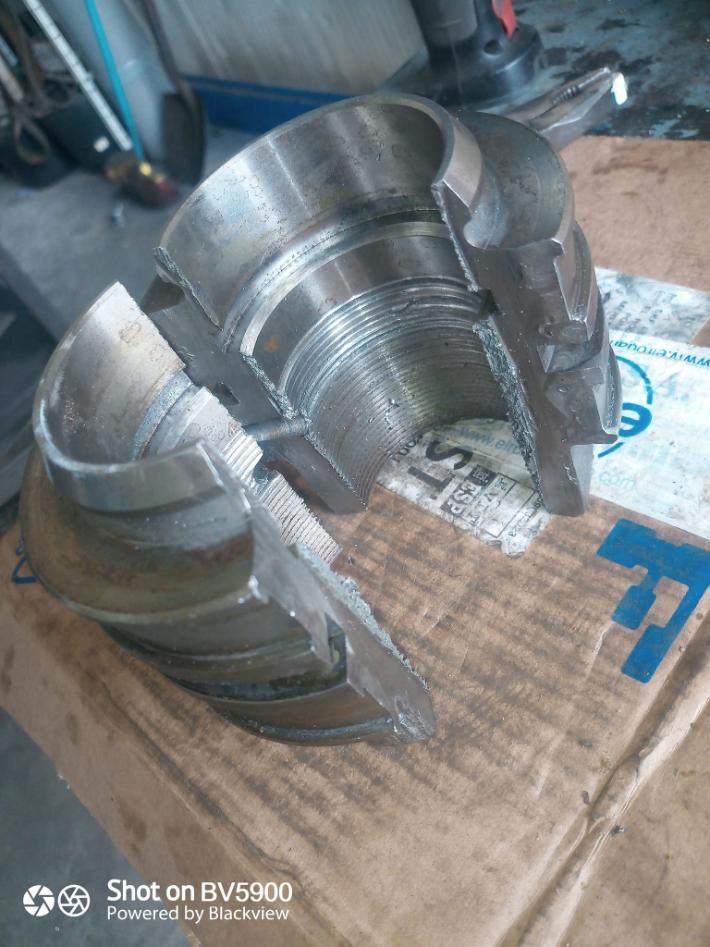 Acoplamiento de metal roto, cortado por la mitad, revelando roscas internas y construcción, sobre superficie de cartón.