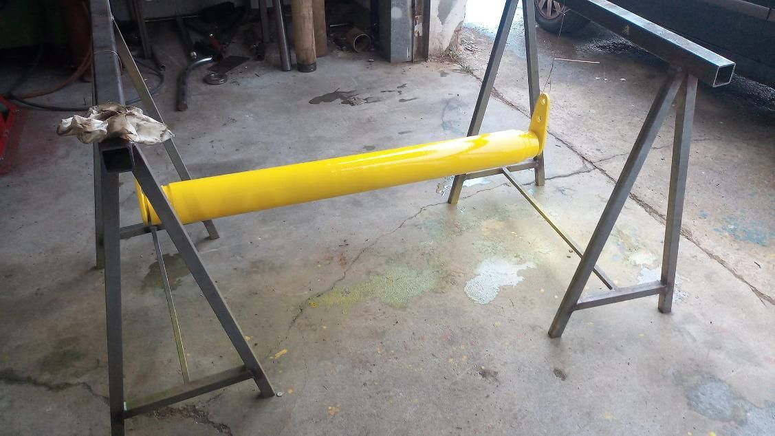 Viga pintada de amarillo sostenida por dos caballetes metálicos en un entorno de taller.