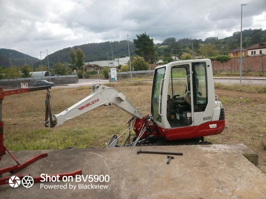 Una miniexcavadora blanca y roja sobre una plataforma de hormigón con una grúa roja