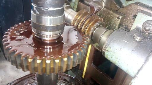 Un engranaje siendo cortado en una máquina, con aceite y un engranaje helicoidal en funcionamiento.