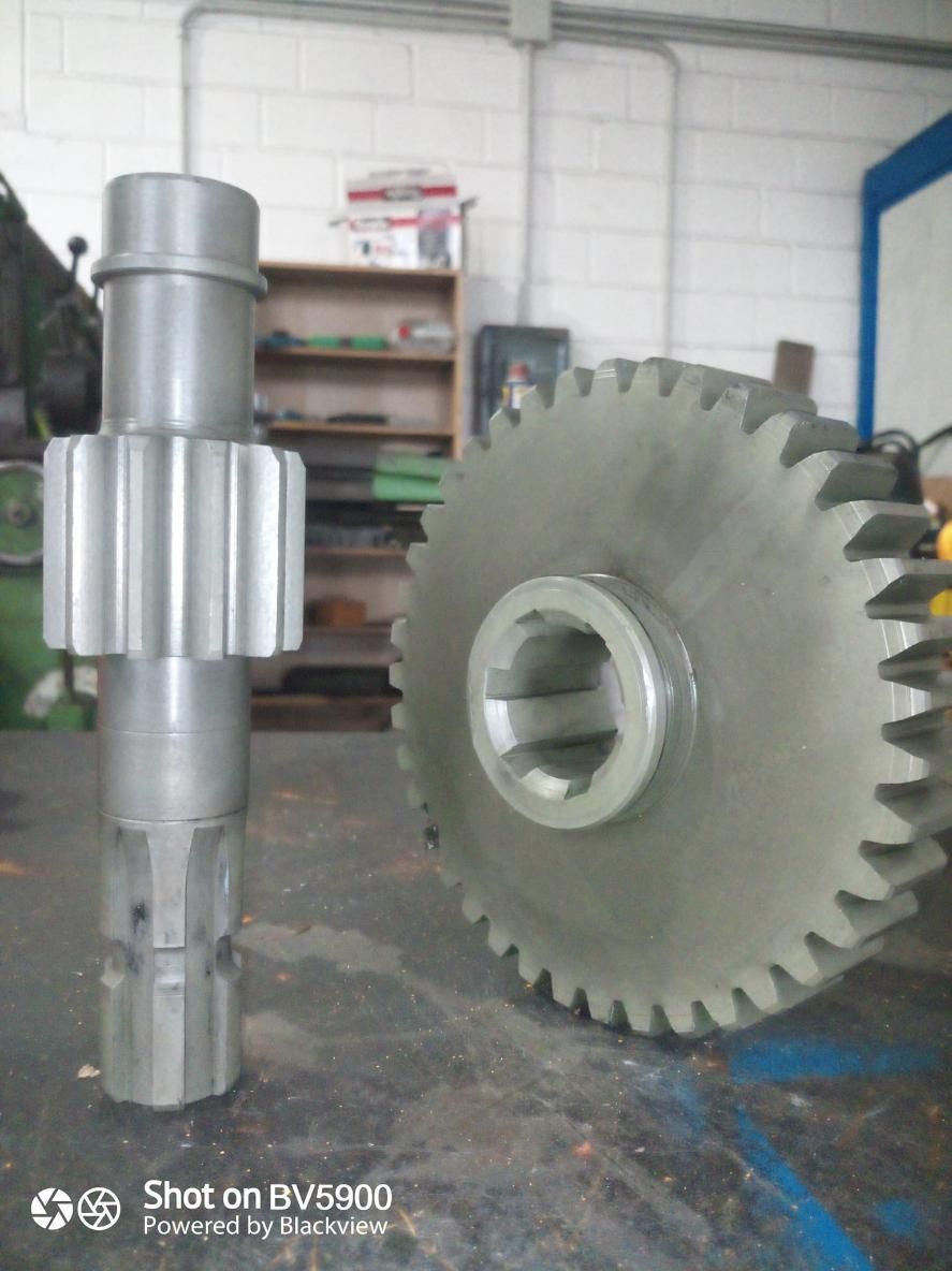 Dos engranajes grises sobre una mesa. Uno es una rueda dentada grande y el otro, un eje de engranaje.