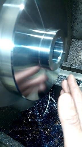 Cilindro de metal siendo mecanizado en un torno; mano en el marco.