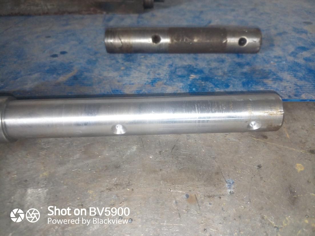 Dos pasadores metálicos cilíndricos con agujeros en la superficie. Uno es más largo y presenta dos abolladuras.