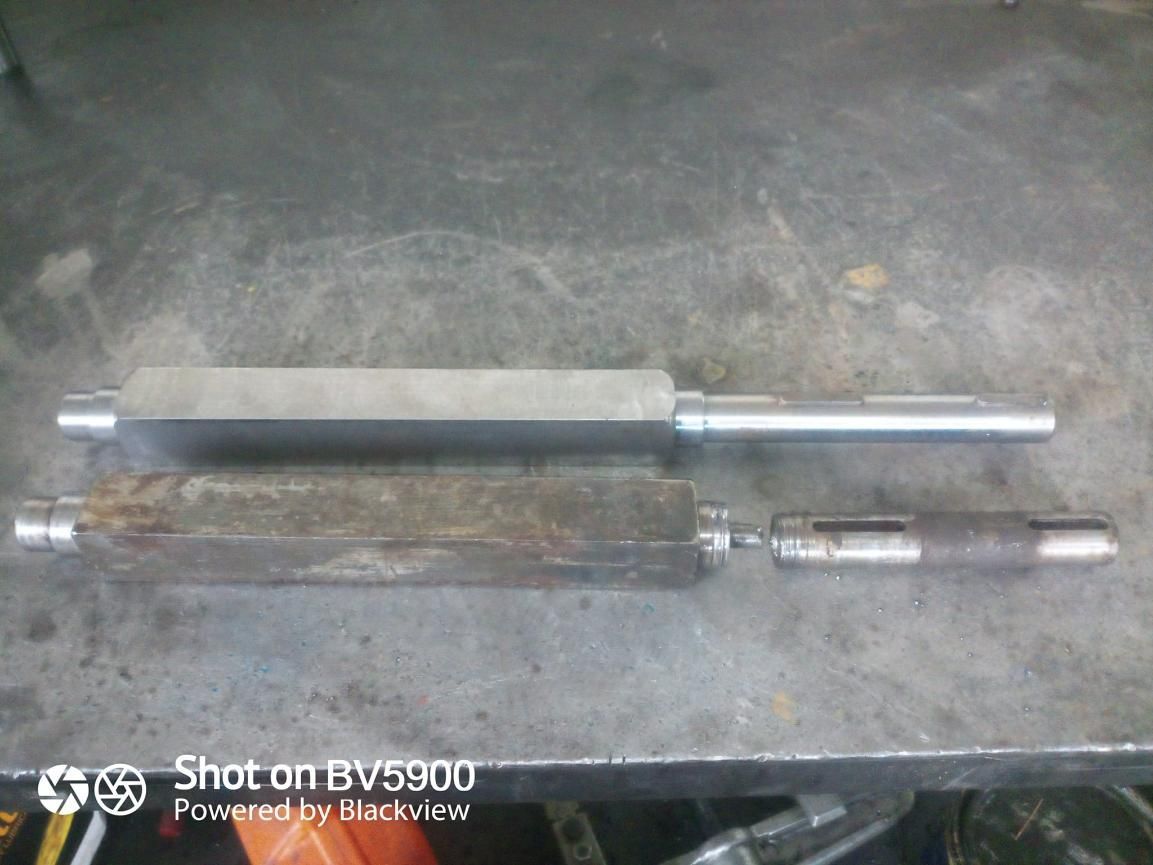 Dos ejes metálicos, uno nuevo y brillante, el otro viejo y oxidado, yacen sobre una superficie metálica.