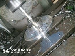 Un taladro de columna mecaniza un objeto metálico, creando virutas de metal.