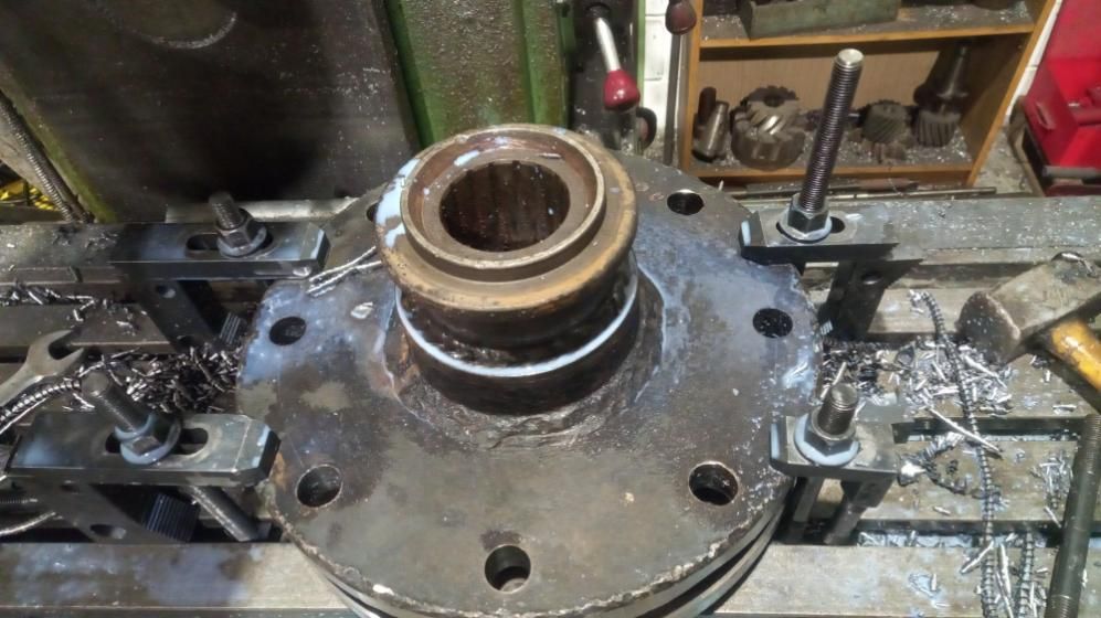 Pieza metálica de gran tamaño sujetada a una fresadora, rodeada de virutas de metal.