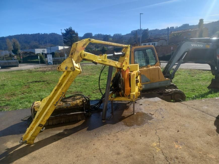 Excavadora amarilla con un brazo acoplado, estacionada afuera en un día soleado.