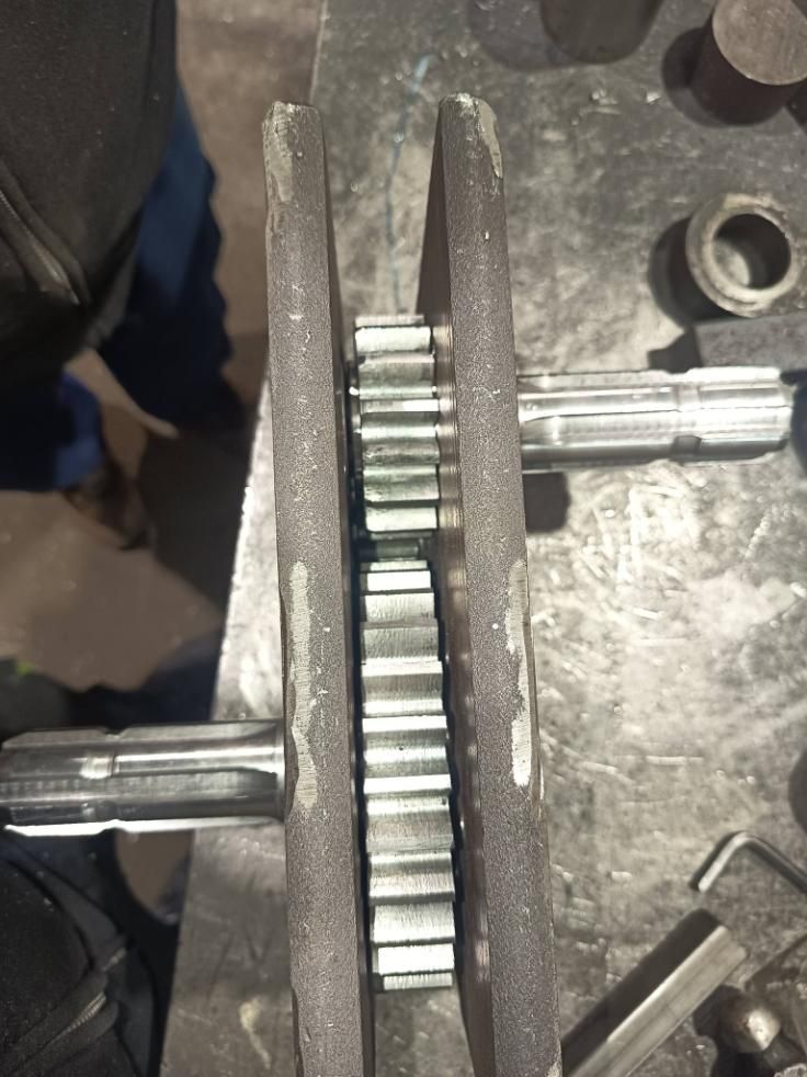 Dos engranajes engranan entre sí entre las mordazas de una prensa, con ejes que se extienden contra un banco de trabajo.