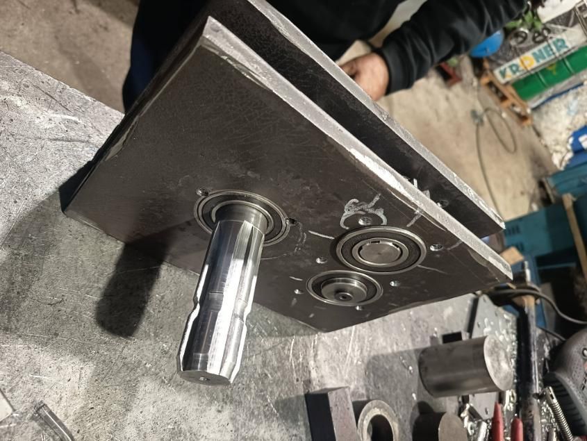 Una pieza de máquina de metal con un eje giratorio y cojinetes, colocada sobre un banco de trabajo.