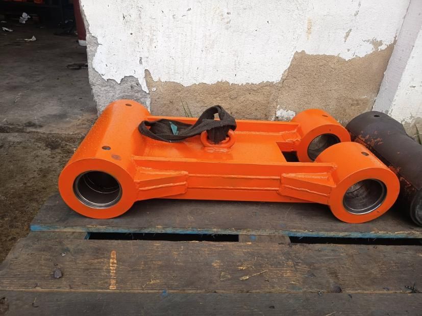 Pieza industrial metálica de color naranja con grandes aberturas cilíndricas, apoyada sobre una superficie de madera.